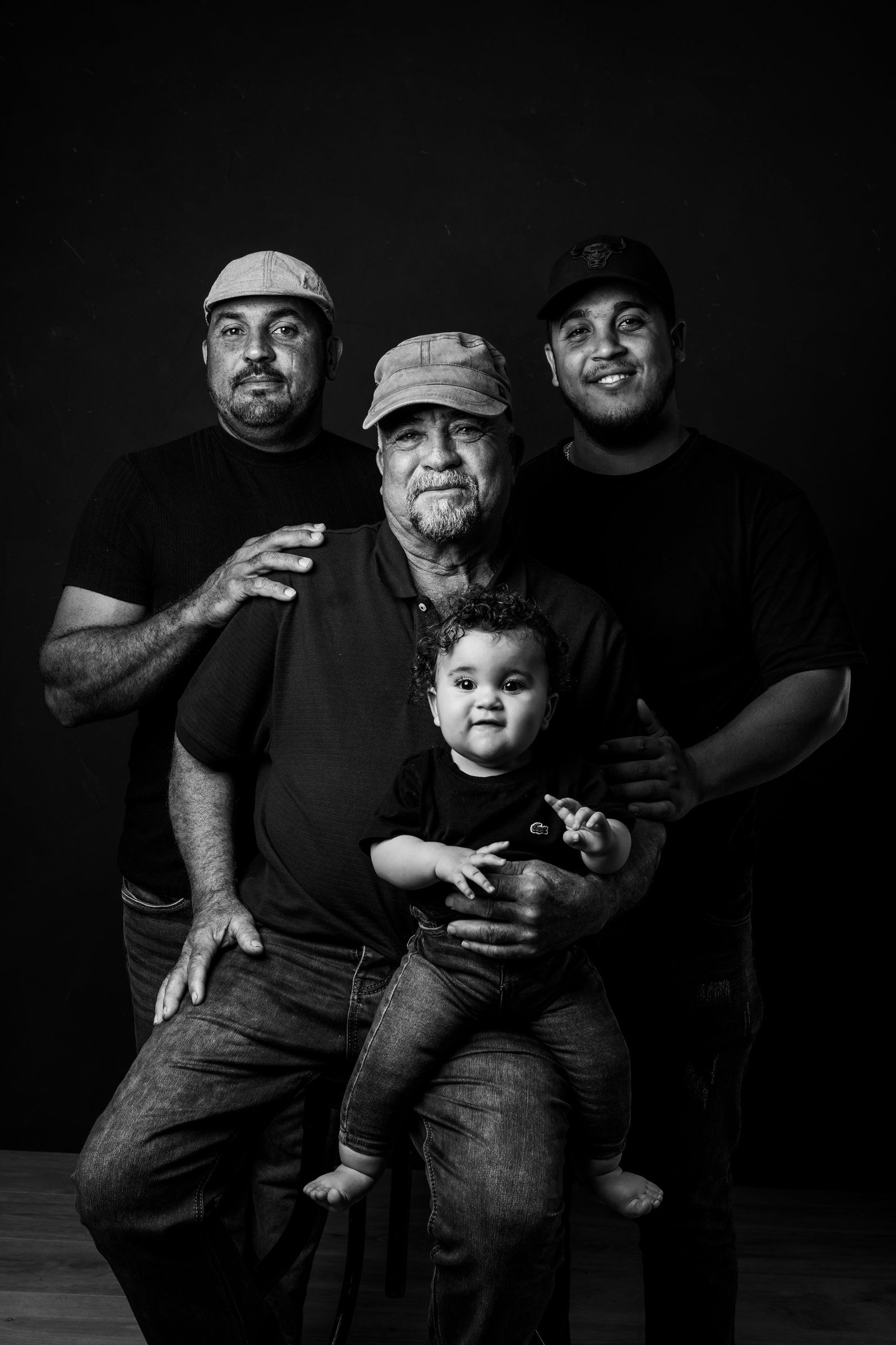 Black and white studio portrait of three generations of men with a baby, showing family bond across ages.
