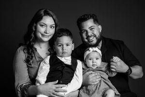 Black and white family portrait of parents with toddler son and baby daughter in bow, studio photo.