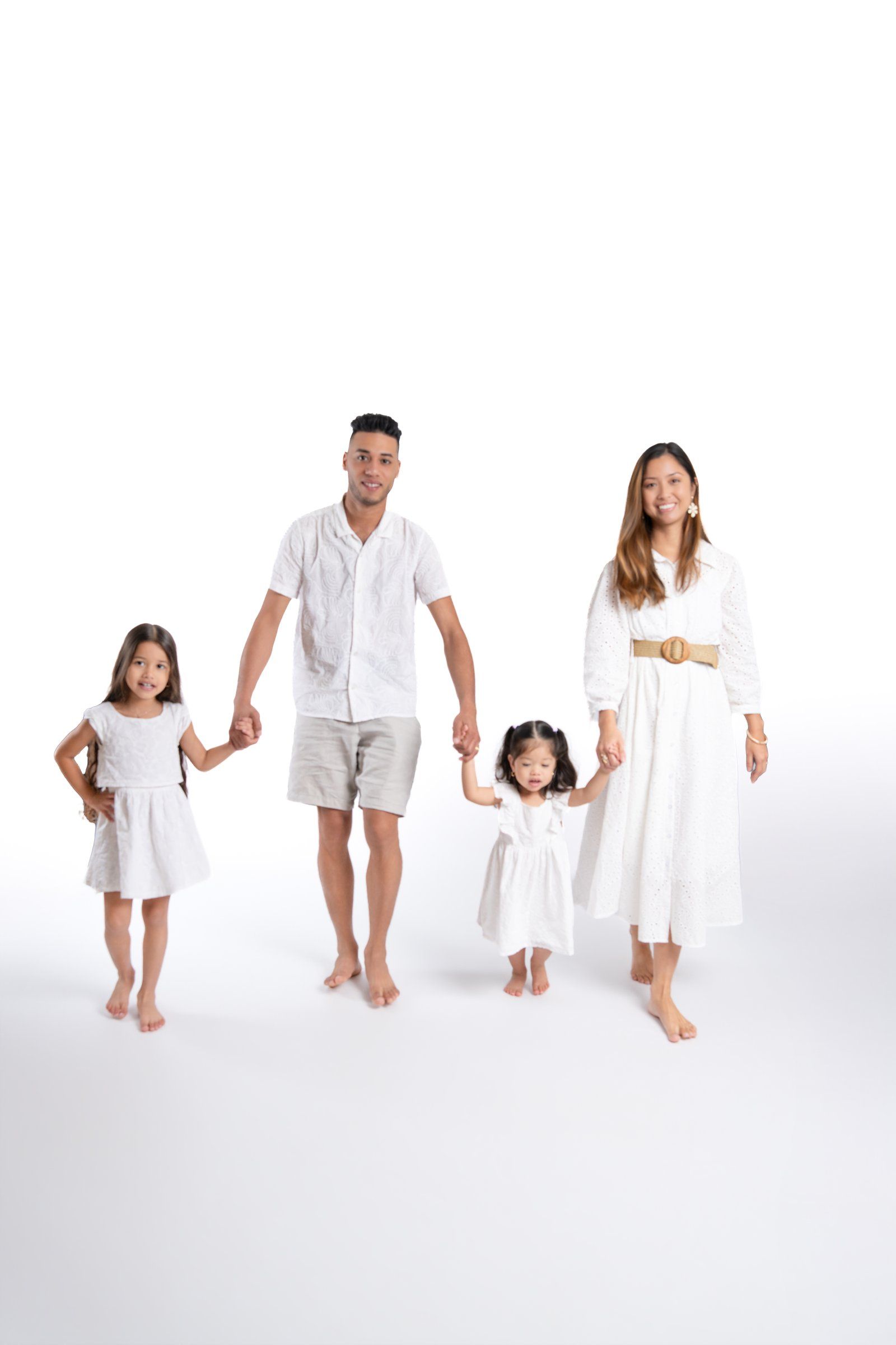 Happy family of four in matching white outfits holding hands against a white background.