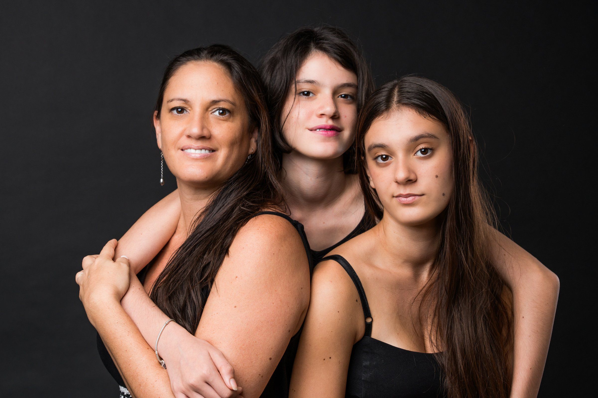Three women pose together against a dark background in a studio portrait photo.