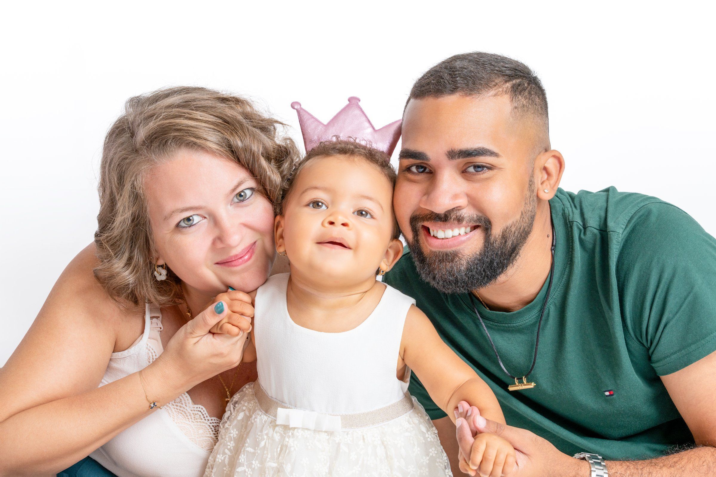 Happy family with parents and baby girl wearing a pink crown in a studio photo.