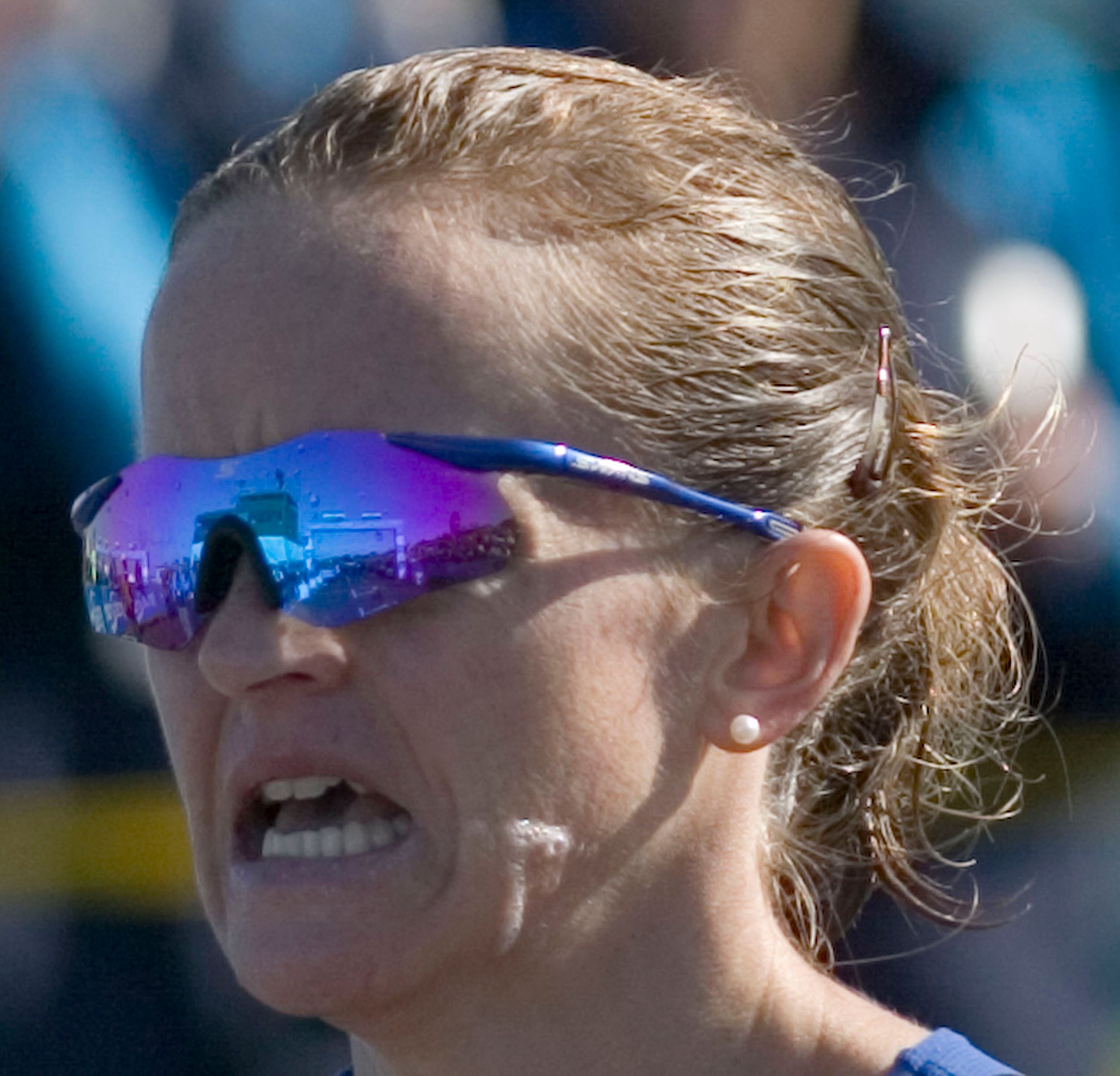 Female athlete wearing blue mirrored sunglasses competing in outdoor road race event.