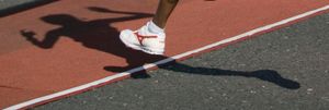 Close-up of athlete's feet in white running shoes casting shadow on red running track.