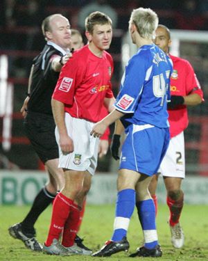 Referee separates players from red and blue teams during heated football match confrontation.
