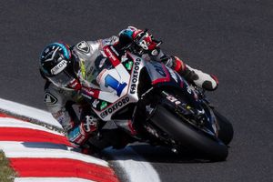 A motorcycle racer on a Buildbase Honda number 1 bike leans into a corner at a British Superbike Championship circuit.