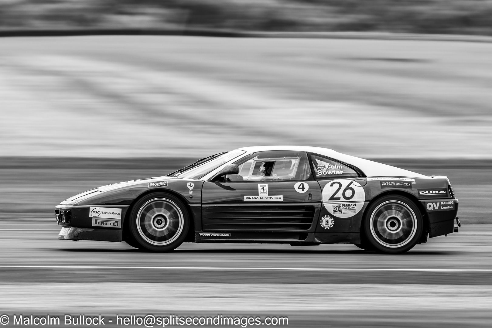 Black and white action shot of a Ferrari 348 race car number 26 speeding along a motorsport circuit track.