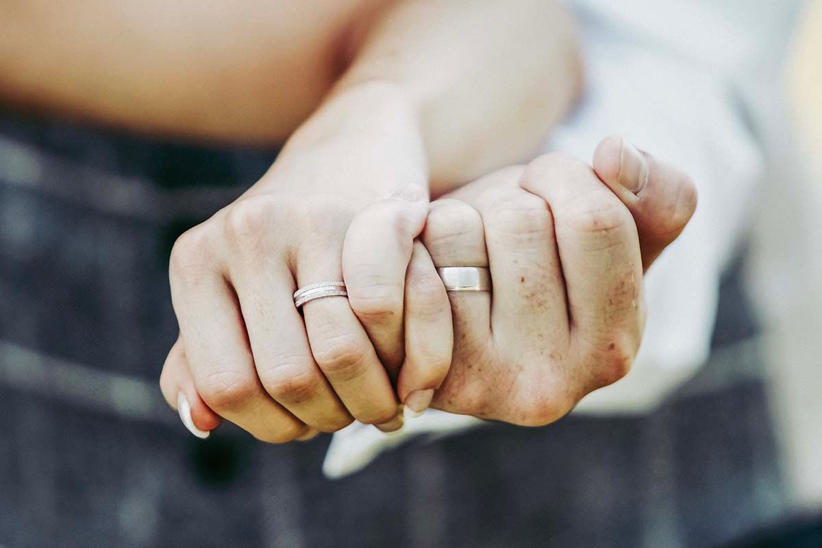 Two hands with wedding rings intertwined, symbolizing love and commitment between a married couple.