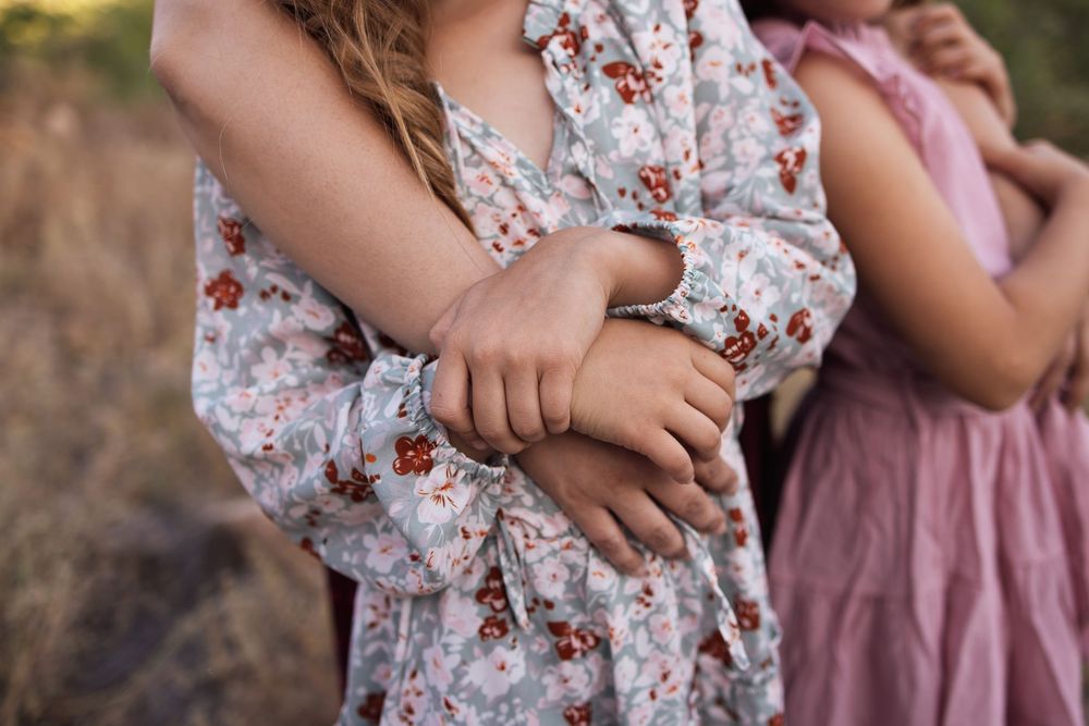 Close-up of two children holding hands, wearing floral and pink dresses in a natural setting.