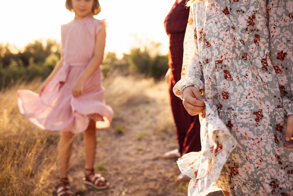 Young girl in pink dress twirling on a sunlit desert path while woman in floral dress holds her hand.