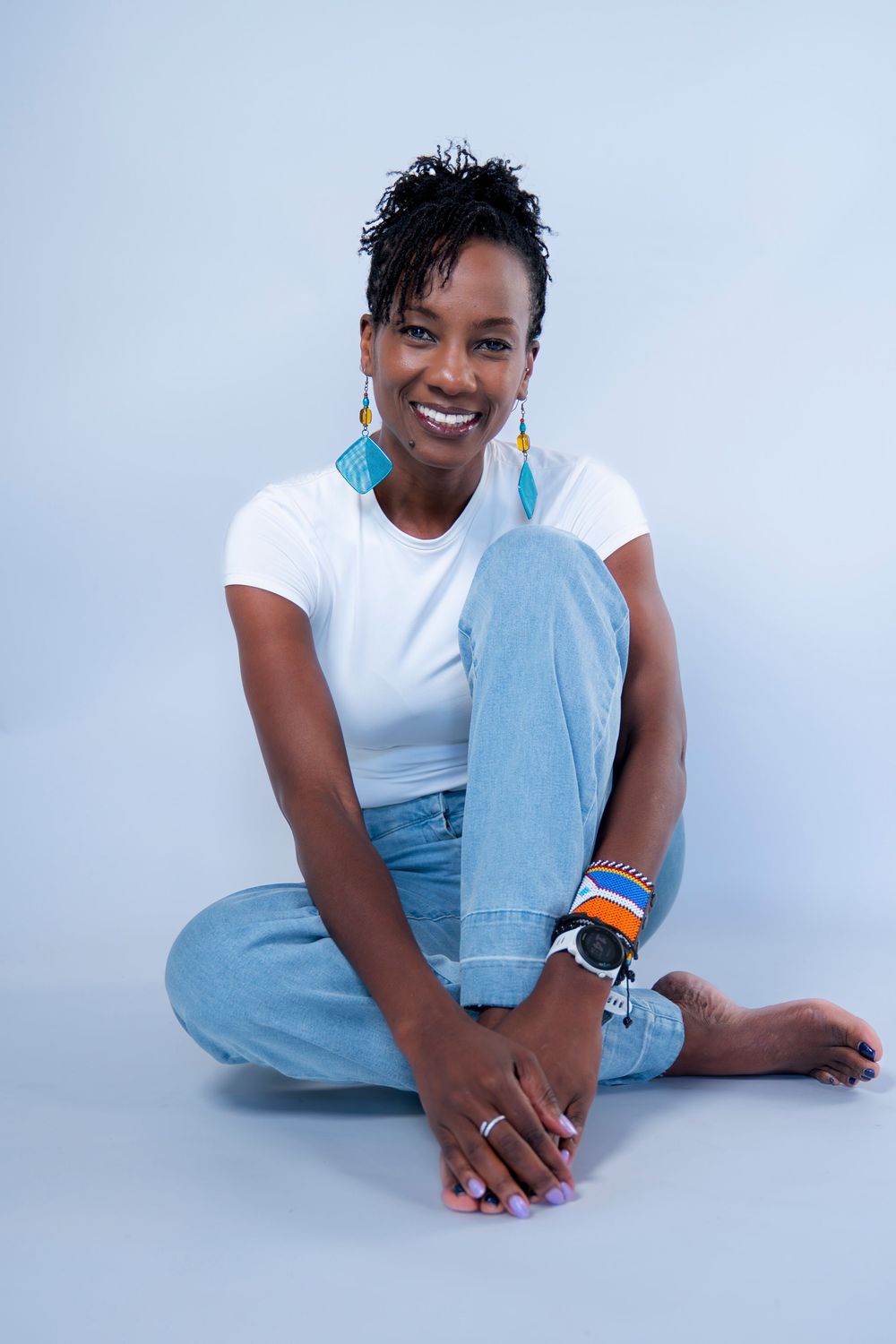 Black woman in white tee and jeans sitting cross-legged smiling with earrings.