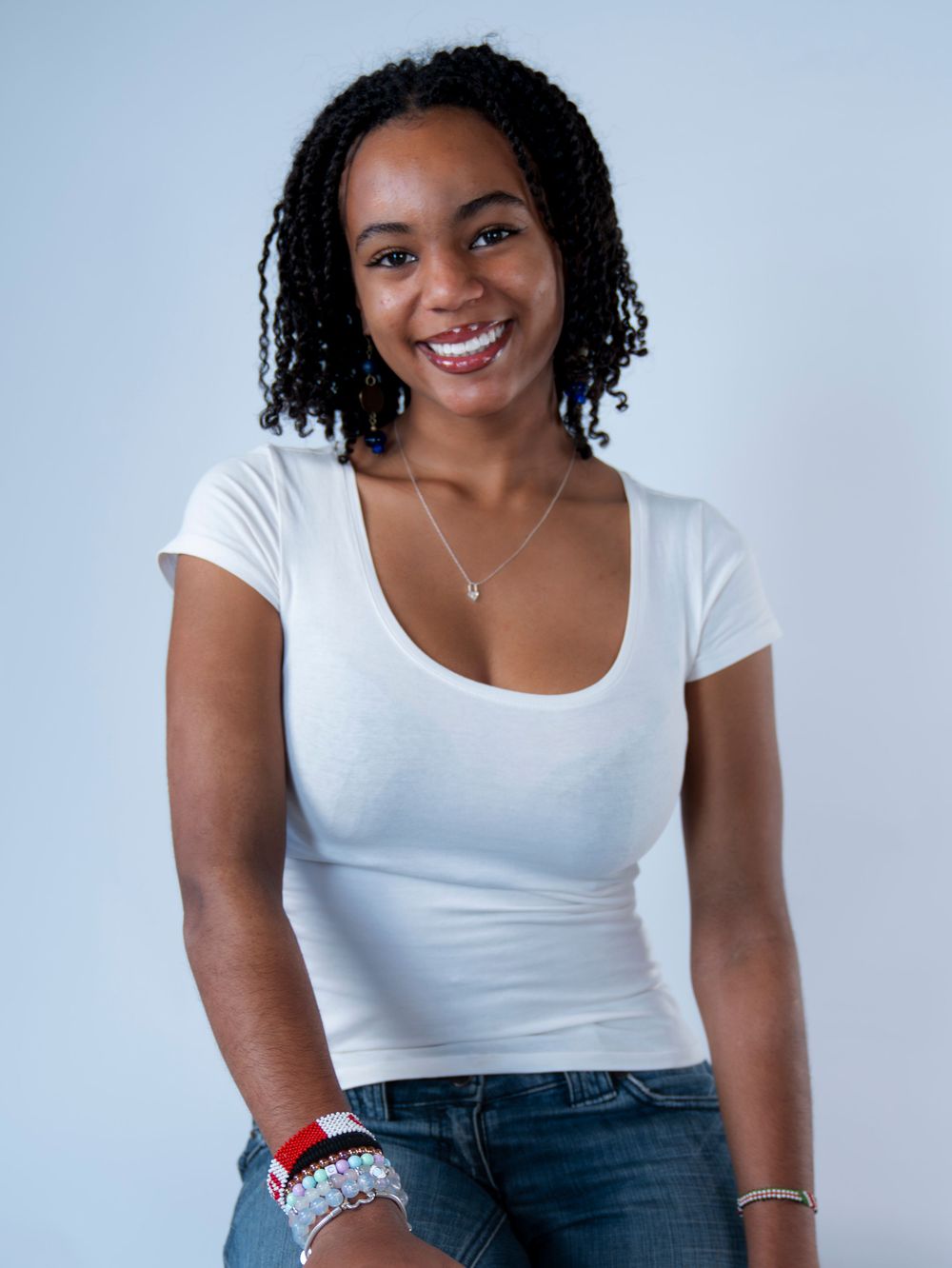Young Black woman in white scoop neck tee smiling with braided hair.