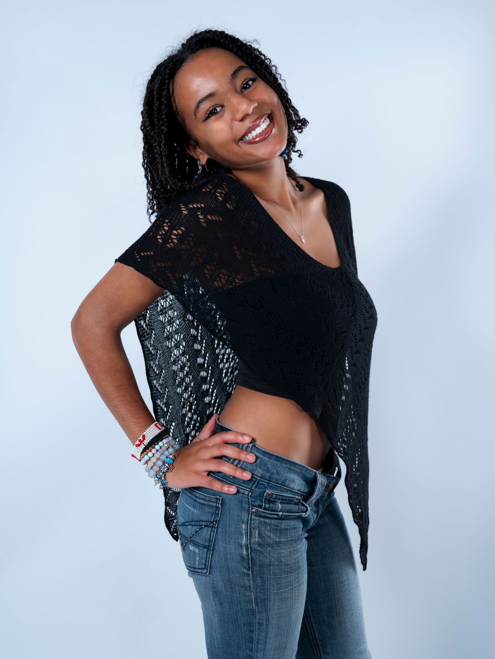 Smiling young Black woman in black lace crop top and jeans posing confidently in a studio setting.