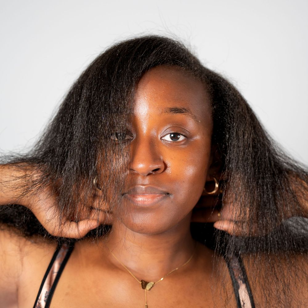 Young African woman with long natural hair posing against light background in casual portrait photo.
