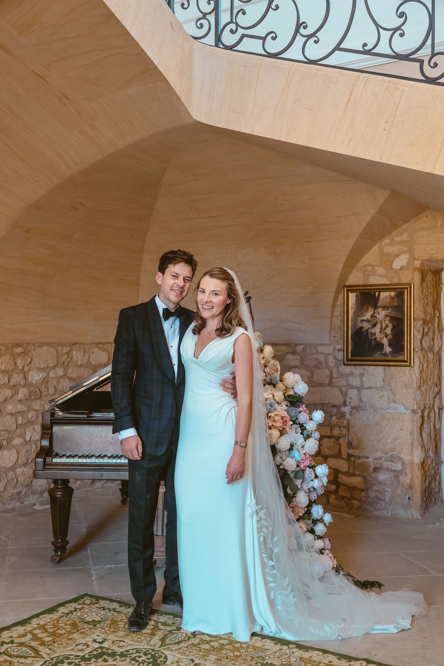 Beth and Matt beside a grand piano decorated with cascading pink and white flowers.