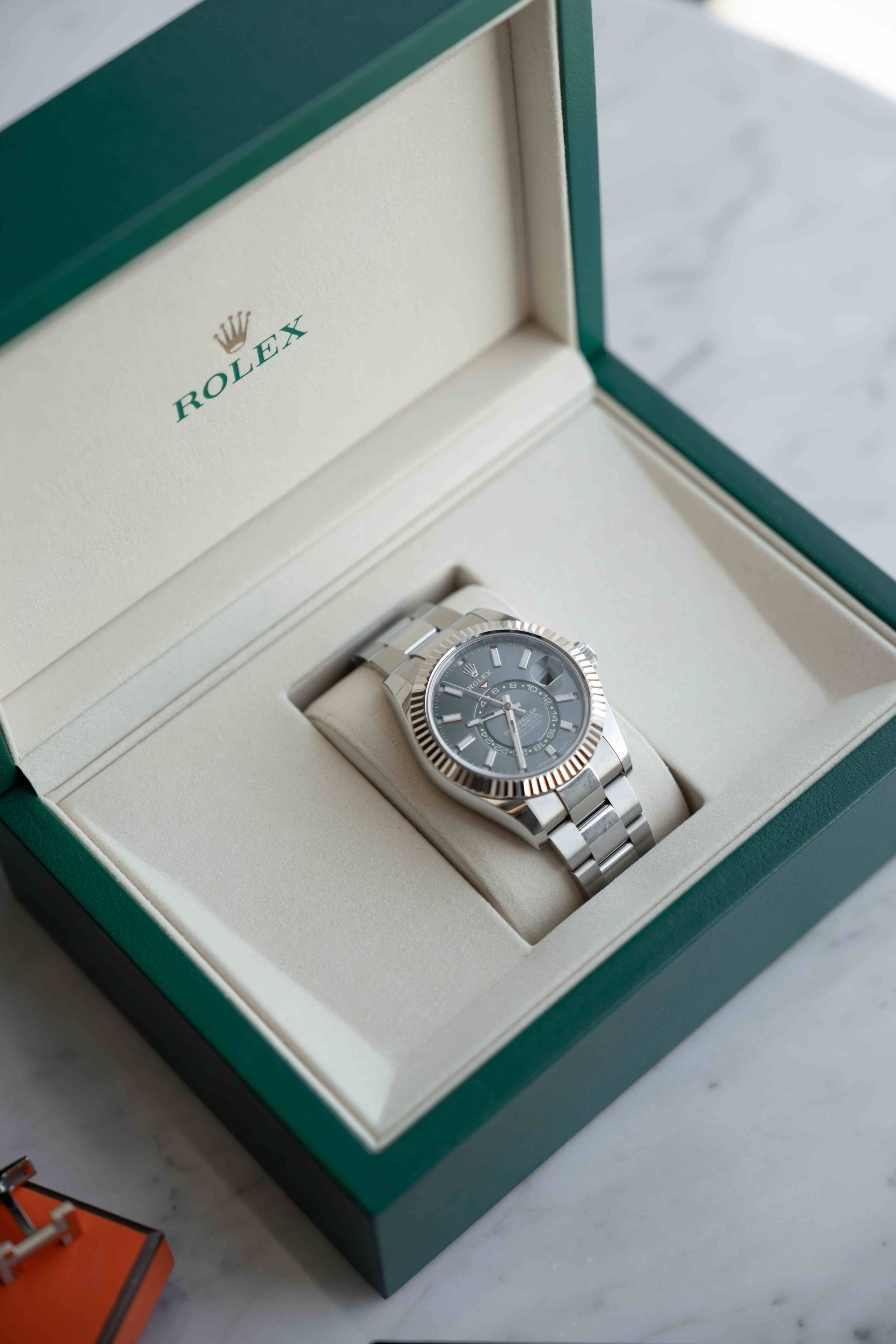 Rolex watch with slate gray dial and oyster bracelet displayed in green luxury gift box on marble surface.