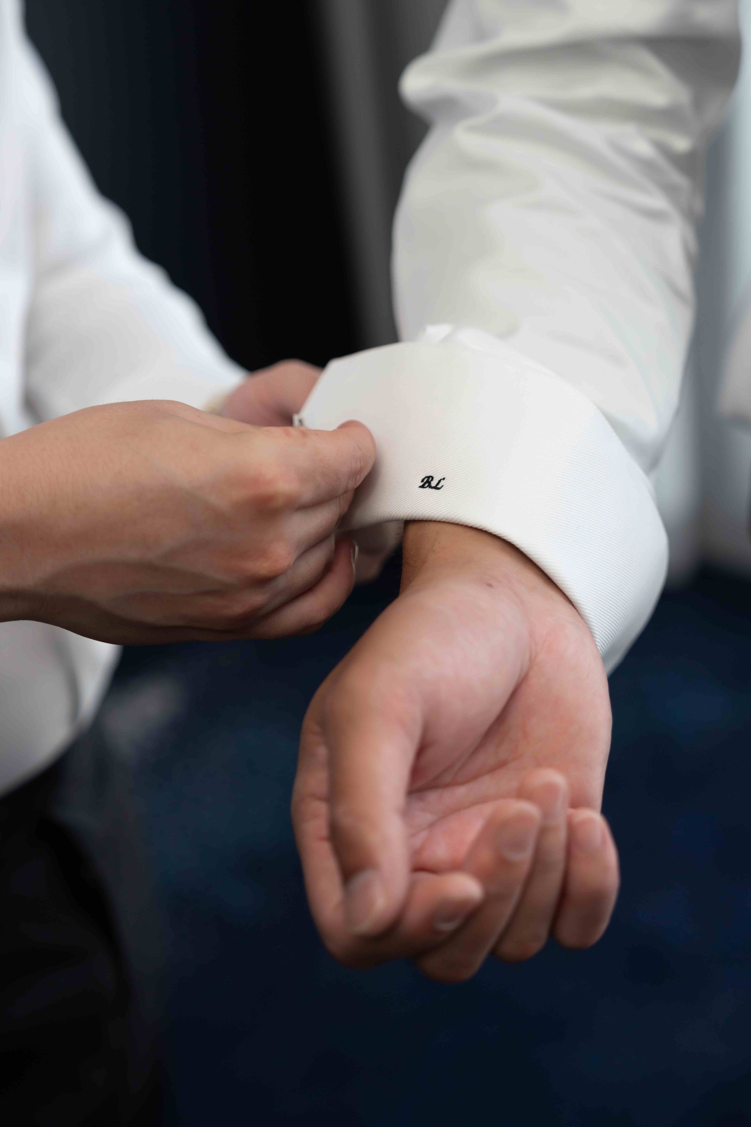 Person fastening monogrammed cufflinks on a white dress shirt sleeve, close-up detail shot.