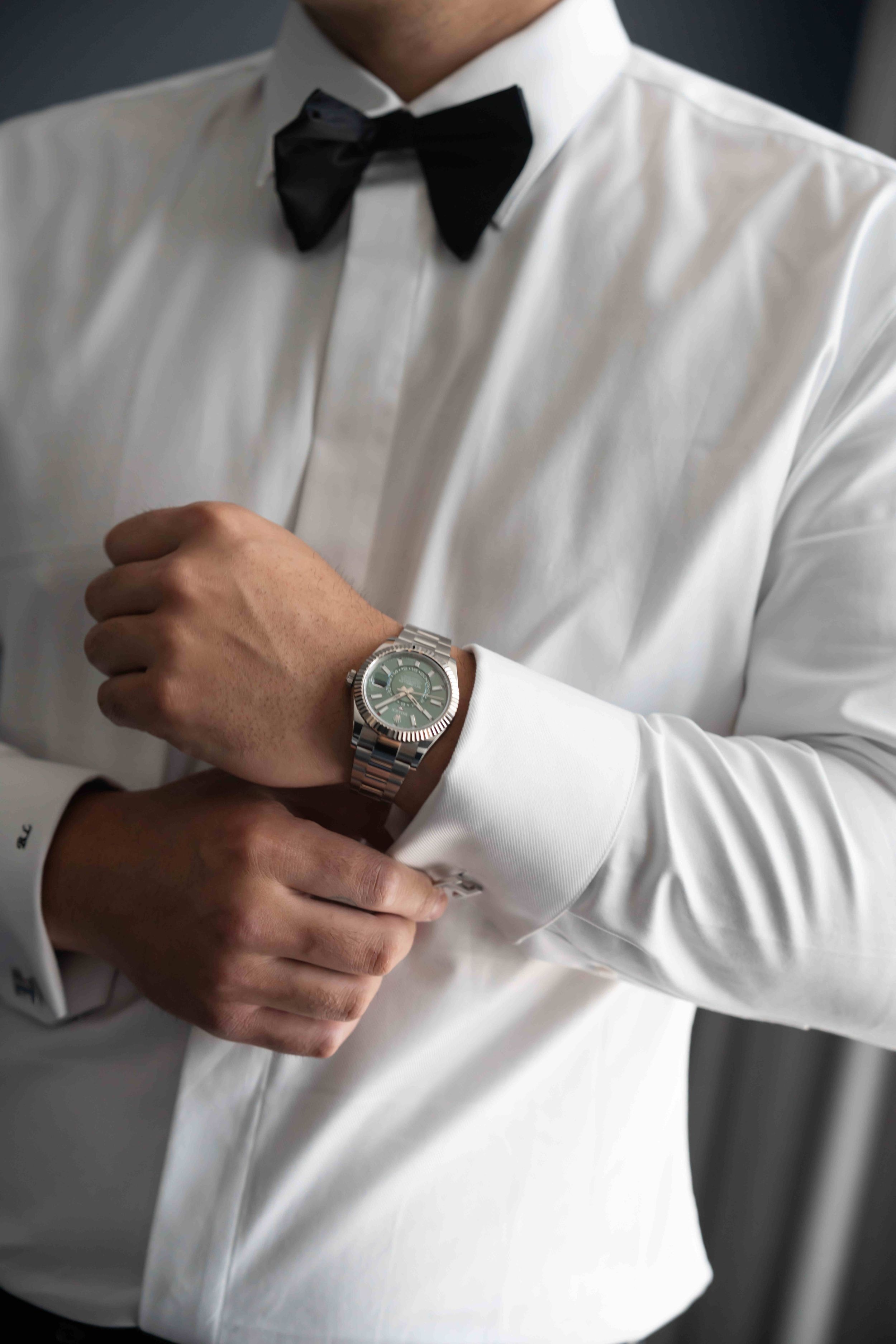 Man in white dress shirt and black bow tie adjusting silver watch on wrist, formal attire close-up.