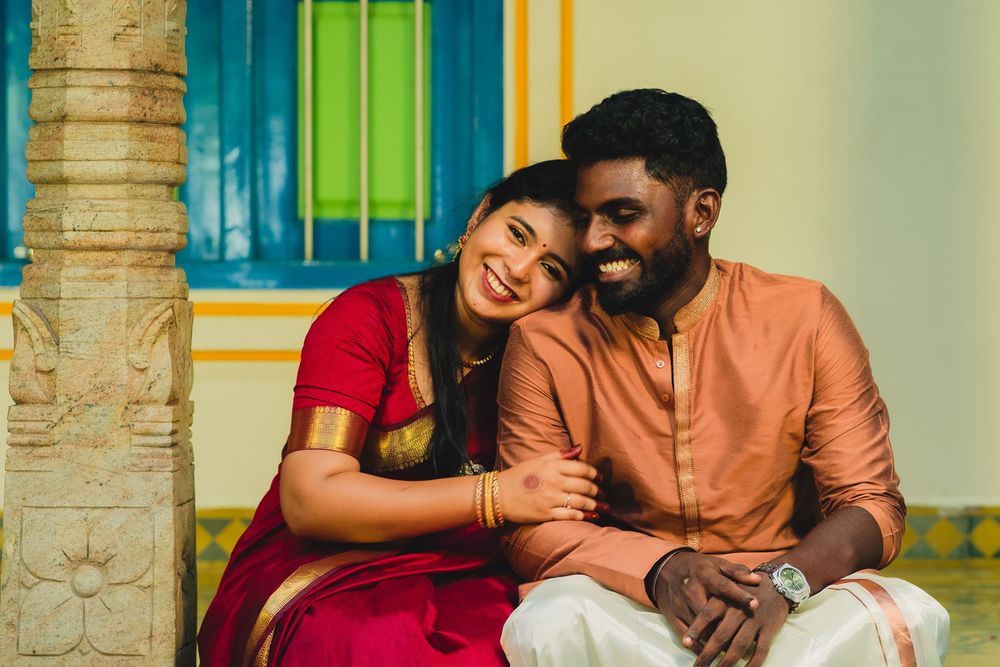 A Tamil couple in traditional attire, woman in red saree and man in orange kurta, sharing a joyful moment together.