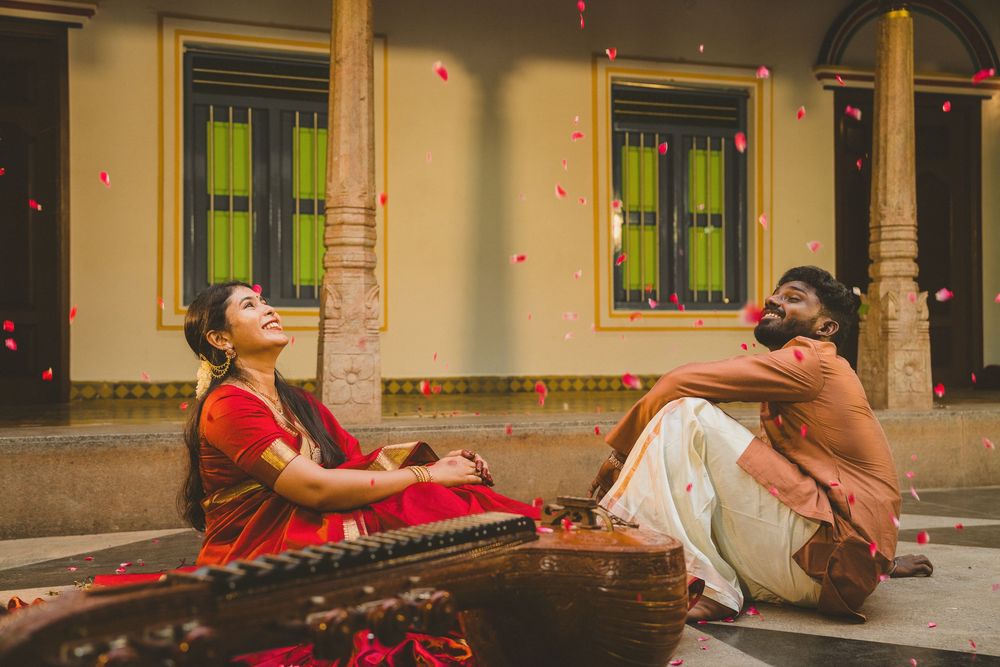 Indian couple in traditional attire sitting together with rose petals falling around them.