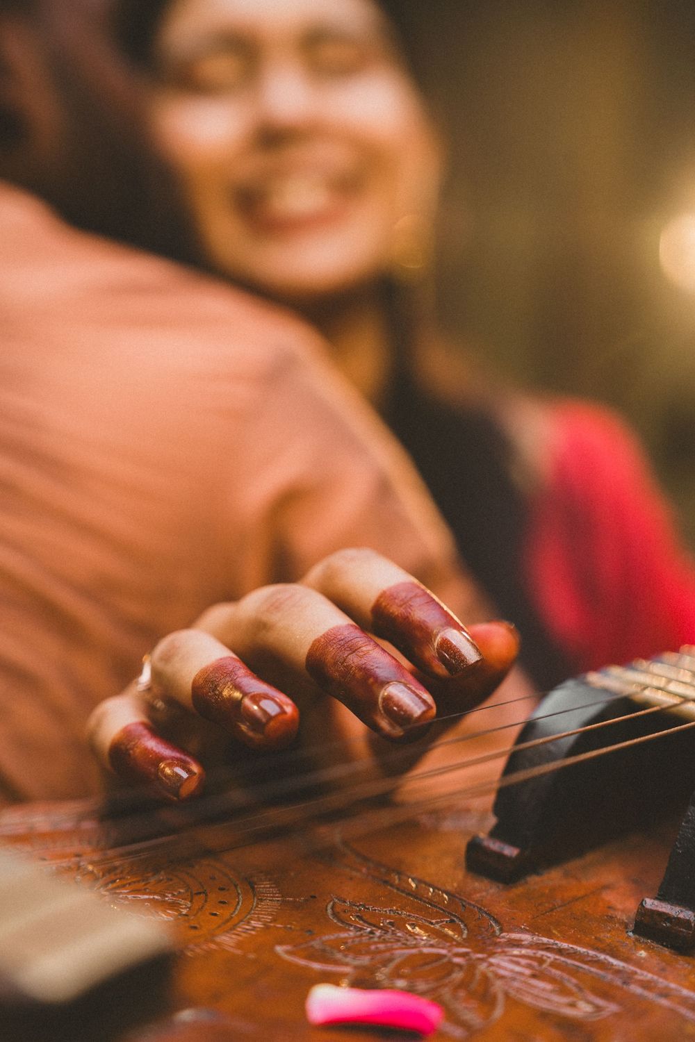 Smiling woman with dark nail polish strumming an ornate acoustic guitar, focused on her hand playing the strings.