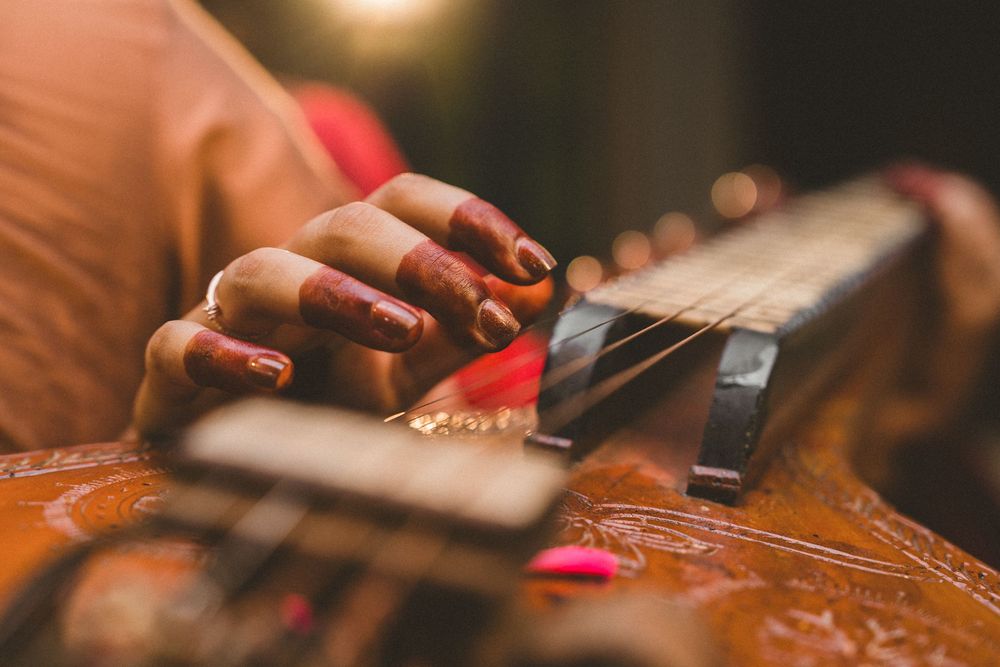 Close-up of a woman with red nails playing a wooden guitar, strumming strings with a pick.