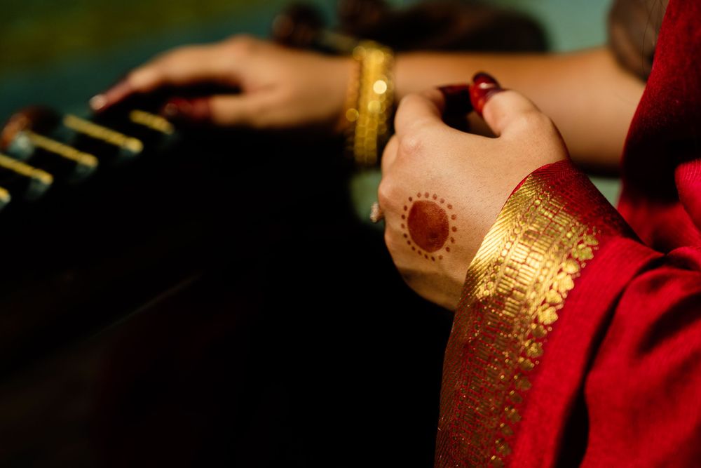 Close-up of woman's hands adorned with henna, gold bangles, and red bridal jewelry during traditional ceremony.