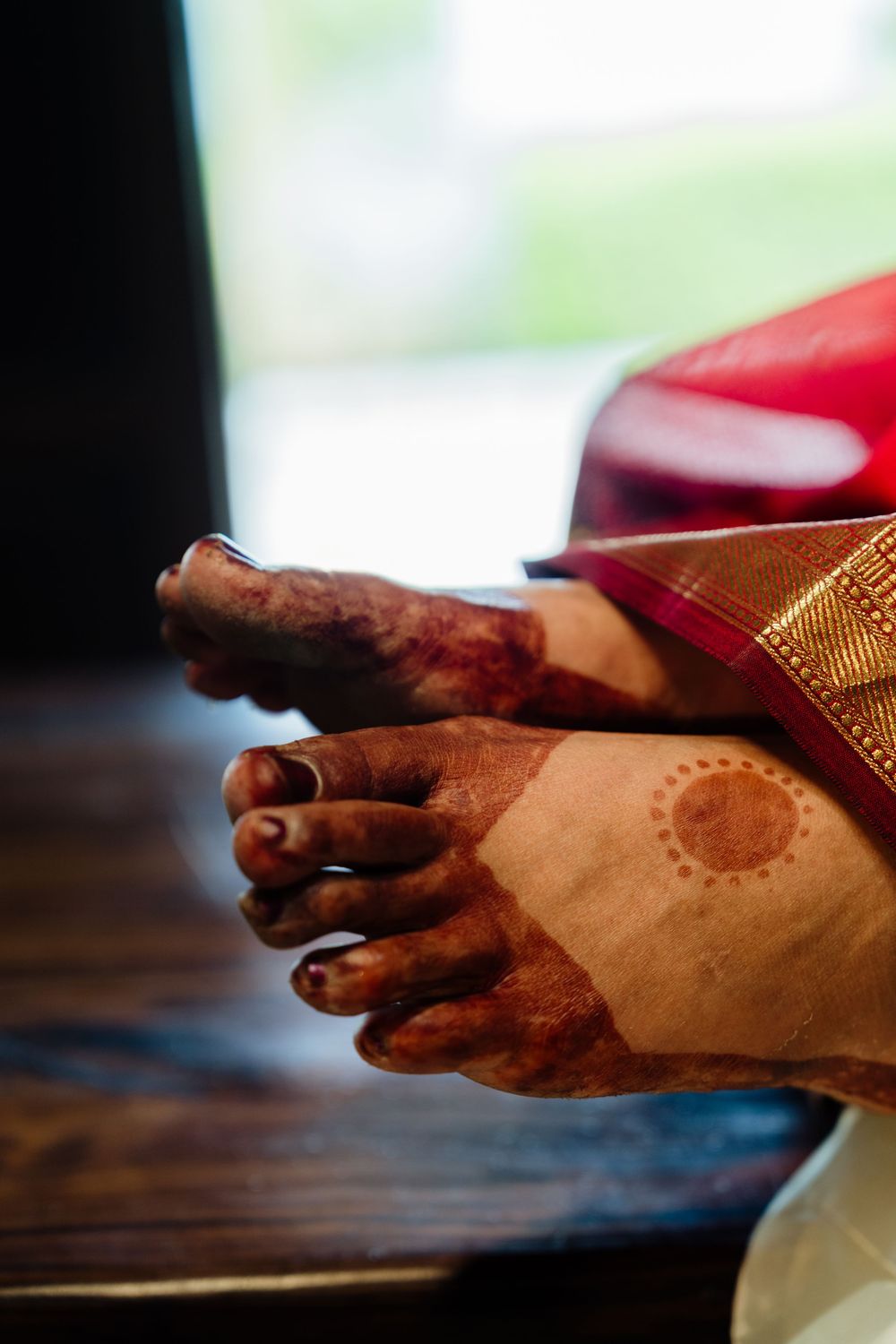 Close-up of Indian bride's feet adorned with intricate henna mehndi design and traditional saree.