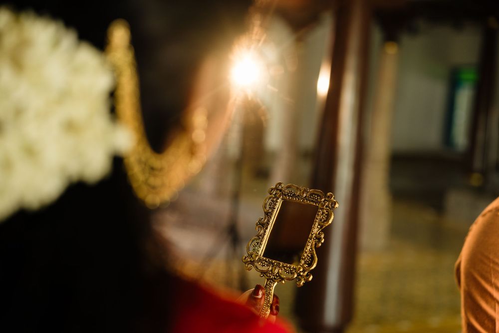A golden ornate hand mirror held up reflecting light during a traditional cultural wedding ceremony.
