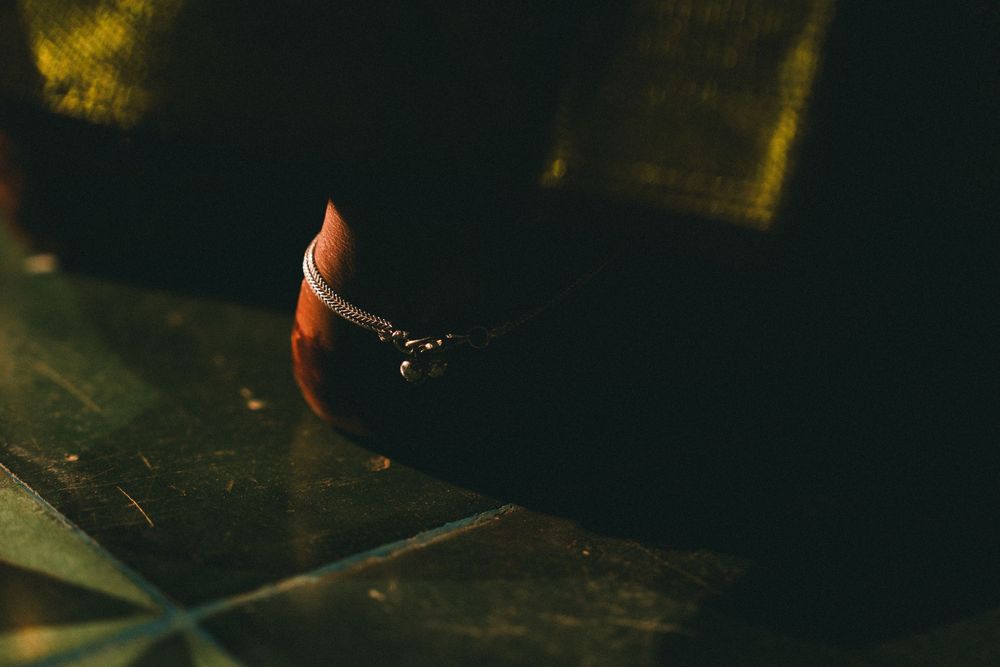 A dark, moody close-up of a small amber glass jar resting on a rustic surface in dim warm light.