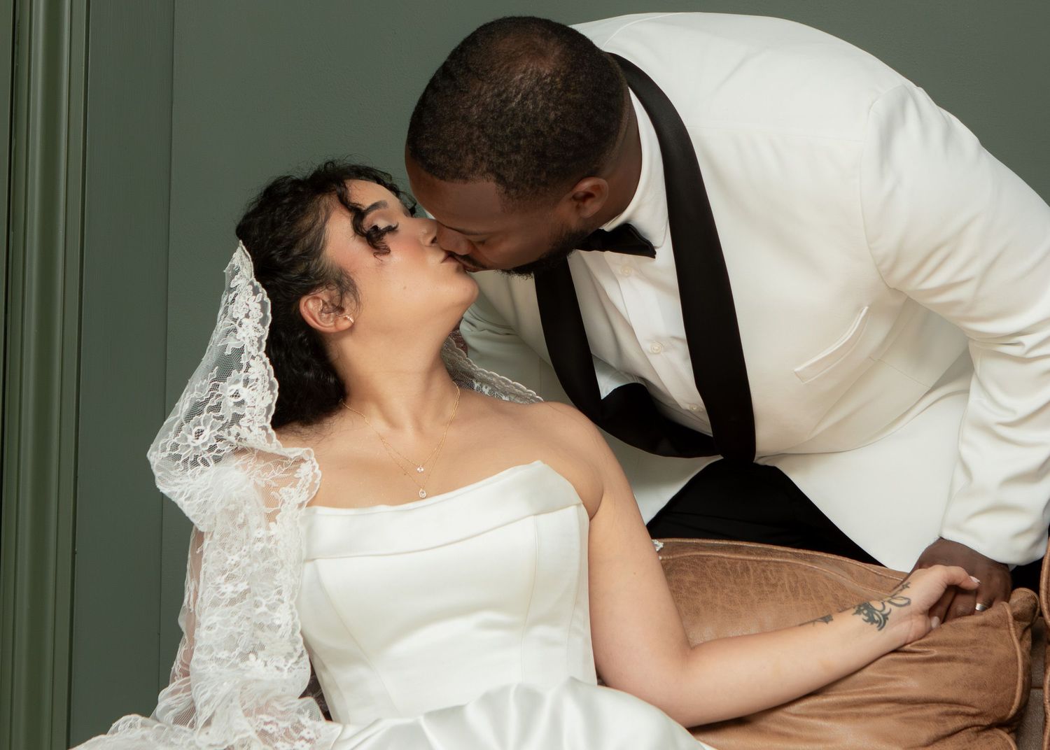 Bride and groom in wedding attire relaxing on a sofa, sharing an intimate moment in elegant white outfits.