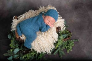 Sleeping newborn swaddled in blue wrap with matching hat in a rustic basket with greenery.