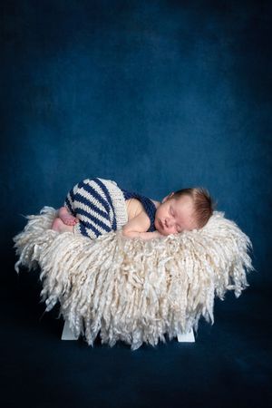 Newborn baby sleeping in a fluffy basket wearing navy blue and white striped knit pants.