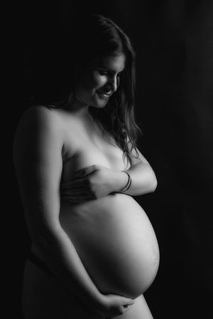 Black and white artistic maternity portrait of smiling pregnant woman cradling bare baby bump.