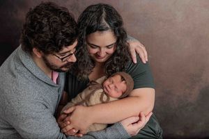 New parents smiling and cradling their sleeping newborn baby in a studio portrait.
