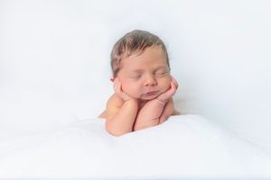 Peaceful newborn baby sleeping with hands under chin on a soft white blanket.