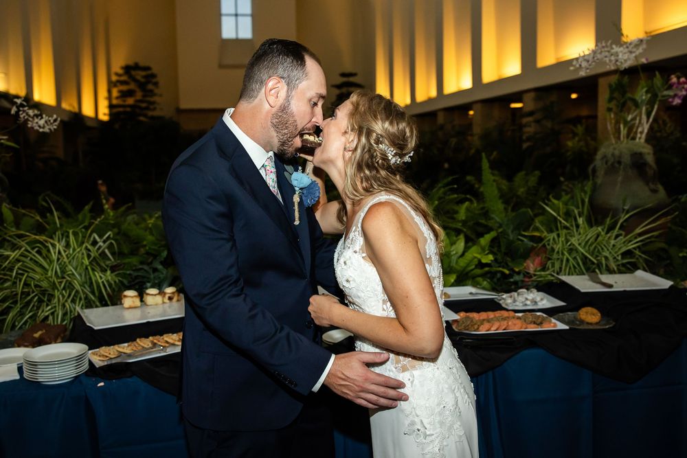Bride and groom share a romantic moment laughing together at their wedding reception near a lush buffet display.