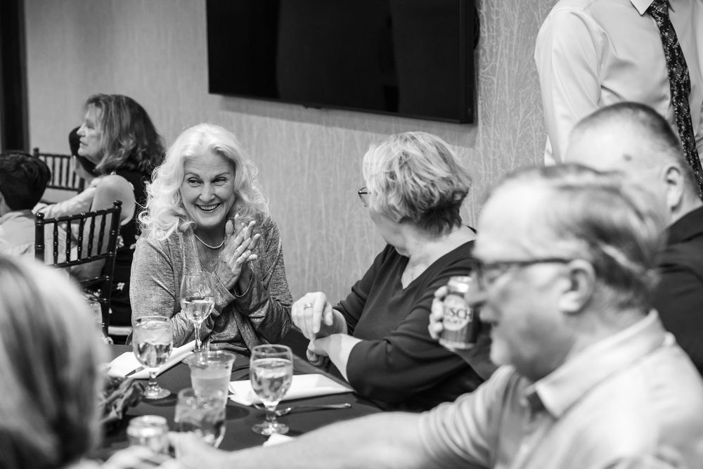 Black and white photo of elderly guests laughing and socializing at a formal dinner event.