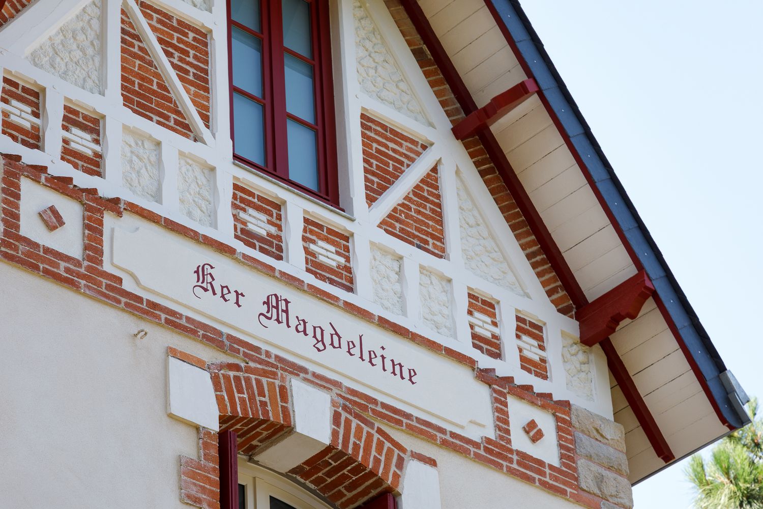 Gros plan sur la façade ornée d'une villa, avec le nom « Ker Magdeleine » inscrit au-dessus d'un décor en briques et de moulures blanches.