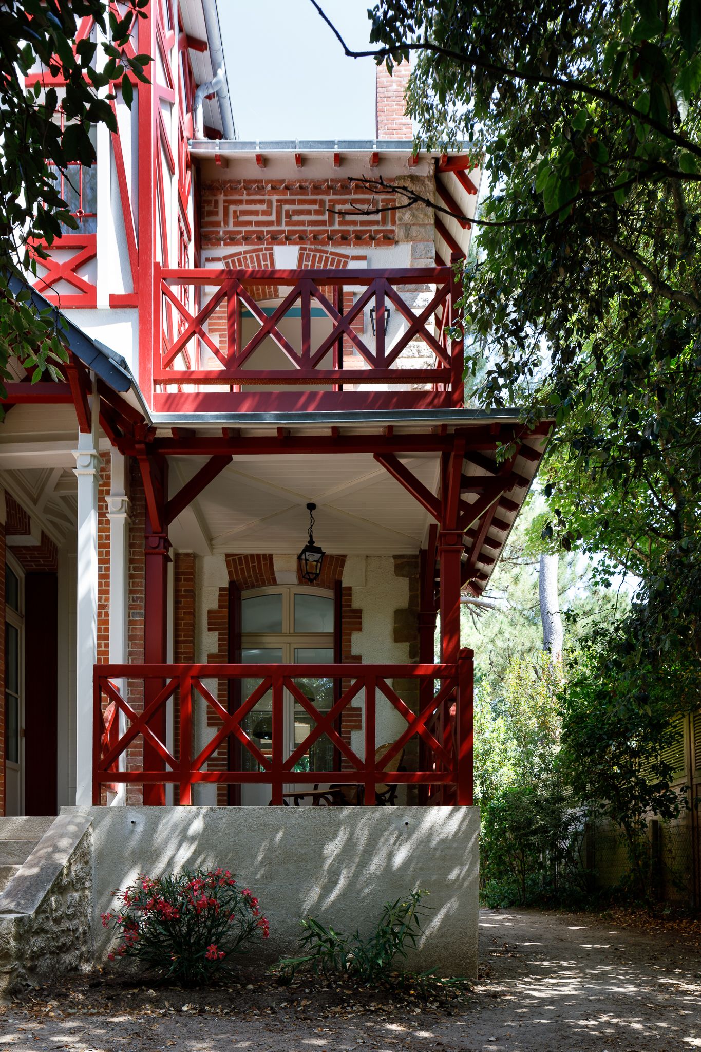 Villa française de style victorien avec balcons en bois rouge, colombages décoratifs et luminaire de porche en forme de lanterne.