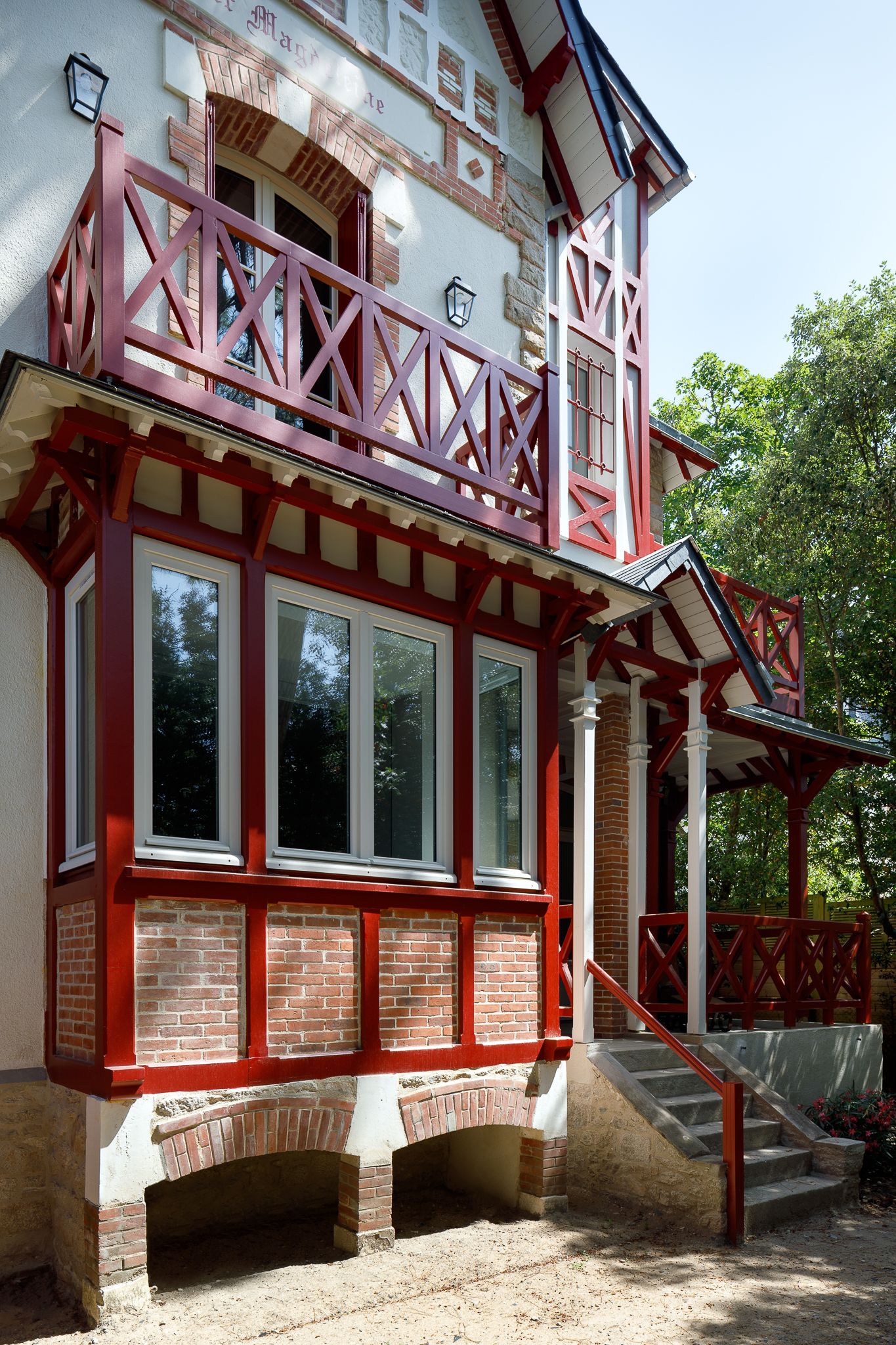 Extérieur d'une villa française historique caractérisé par des pans de bois rouges, des détails en brique, de grandes fenêtres et un balcon