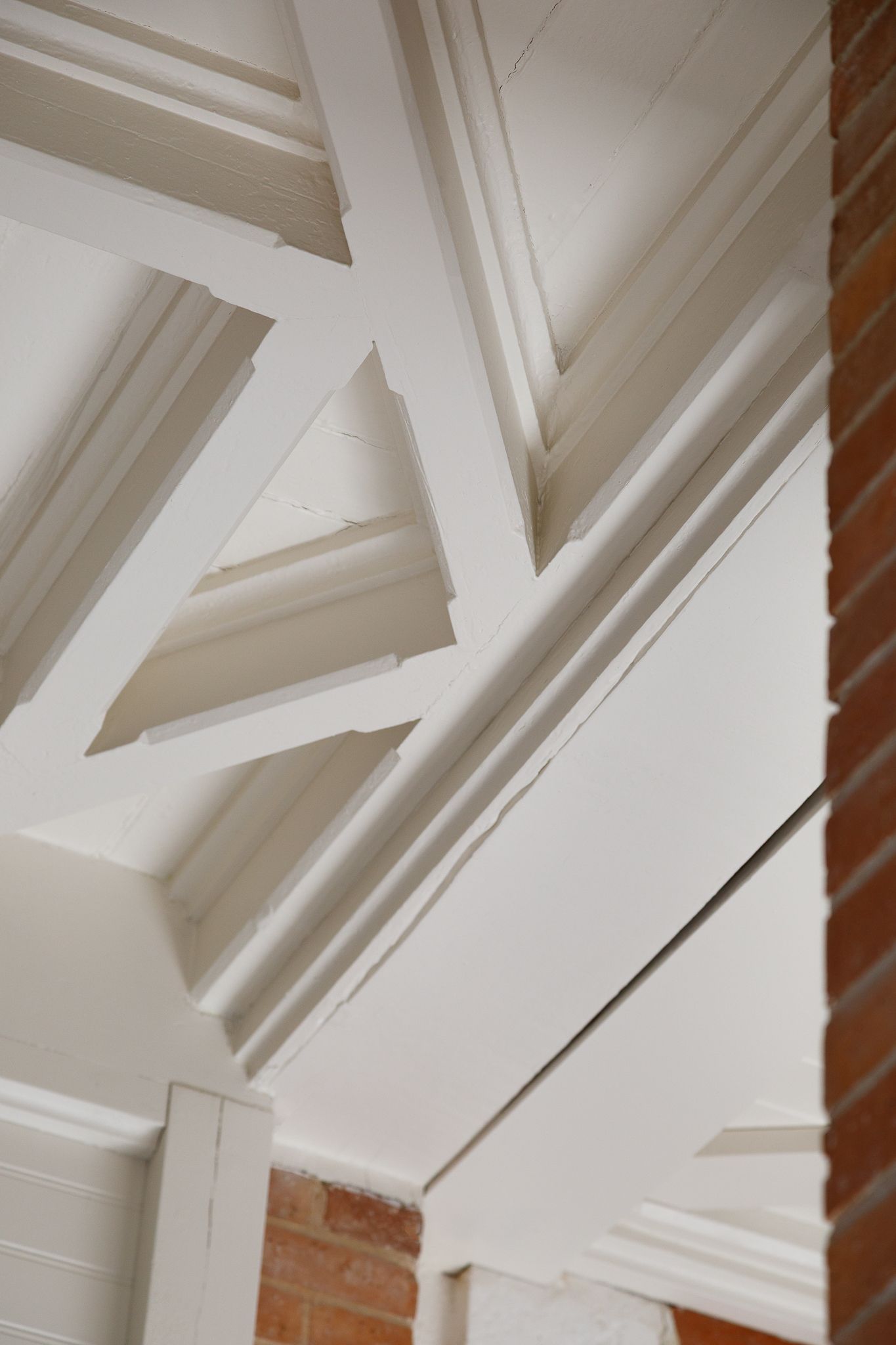 Fermes de toiture en bois peint en blanc, avec un détail architectural constitué d'un mur en briques apparentes.