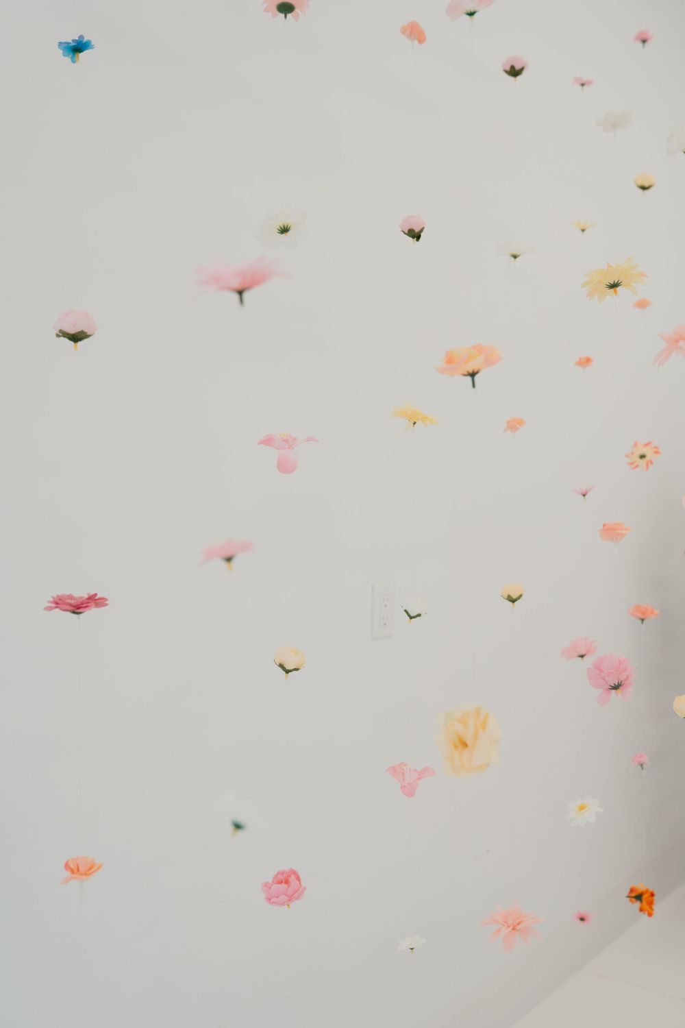 White wall and ceiling decorated with scattered colorful pressed flower stickers in pink, yellow, orange, and blue hues.
