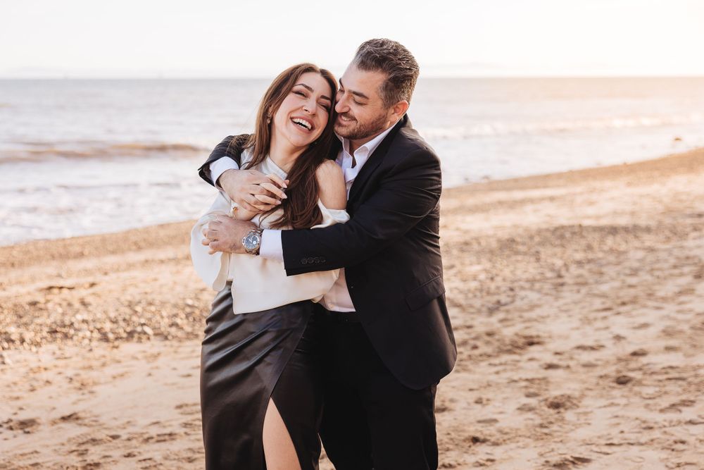 A joyful embrace on the beach at sunset with waves crashing in the background.
