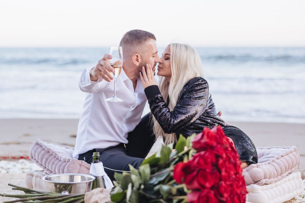 Romantic beach picnic scene with red roses and cozy blankets at sunset.