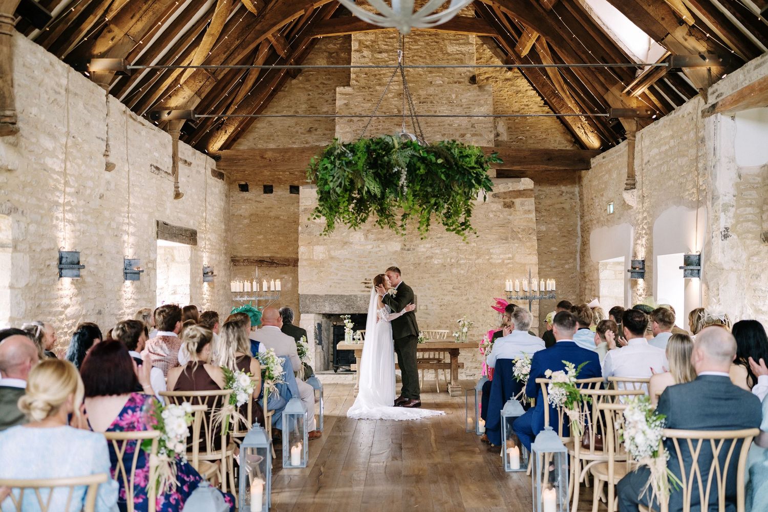 Bride and groom say their vows under hanging greenery in the stone barn at Ivy Lodge Yardspace near Cirencester, by Stu Tucker Photography