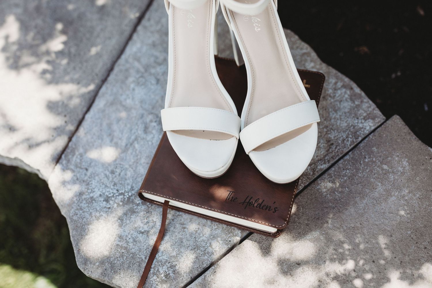 White bridal shoes resting on a brown bible book on a stone surface.