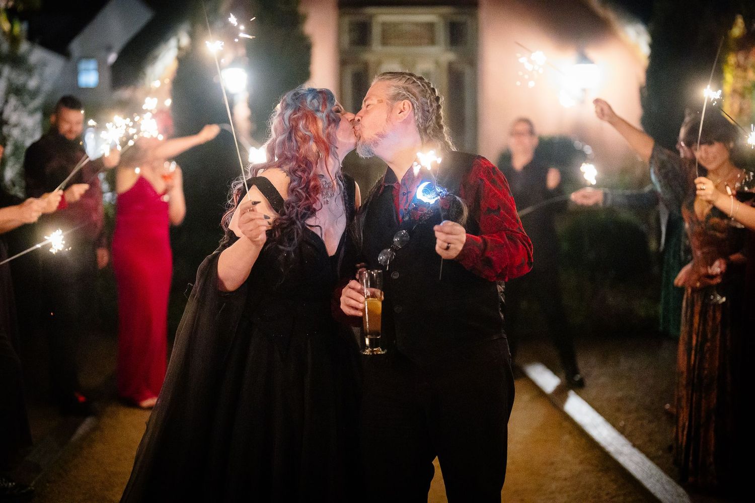 Bride and groom kissing as guests hold sparklers outside the pink cottage at Le Petit Chateau