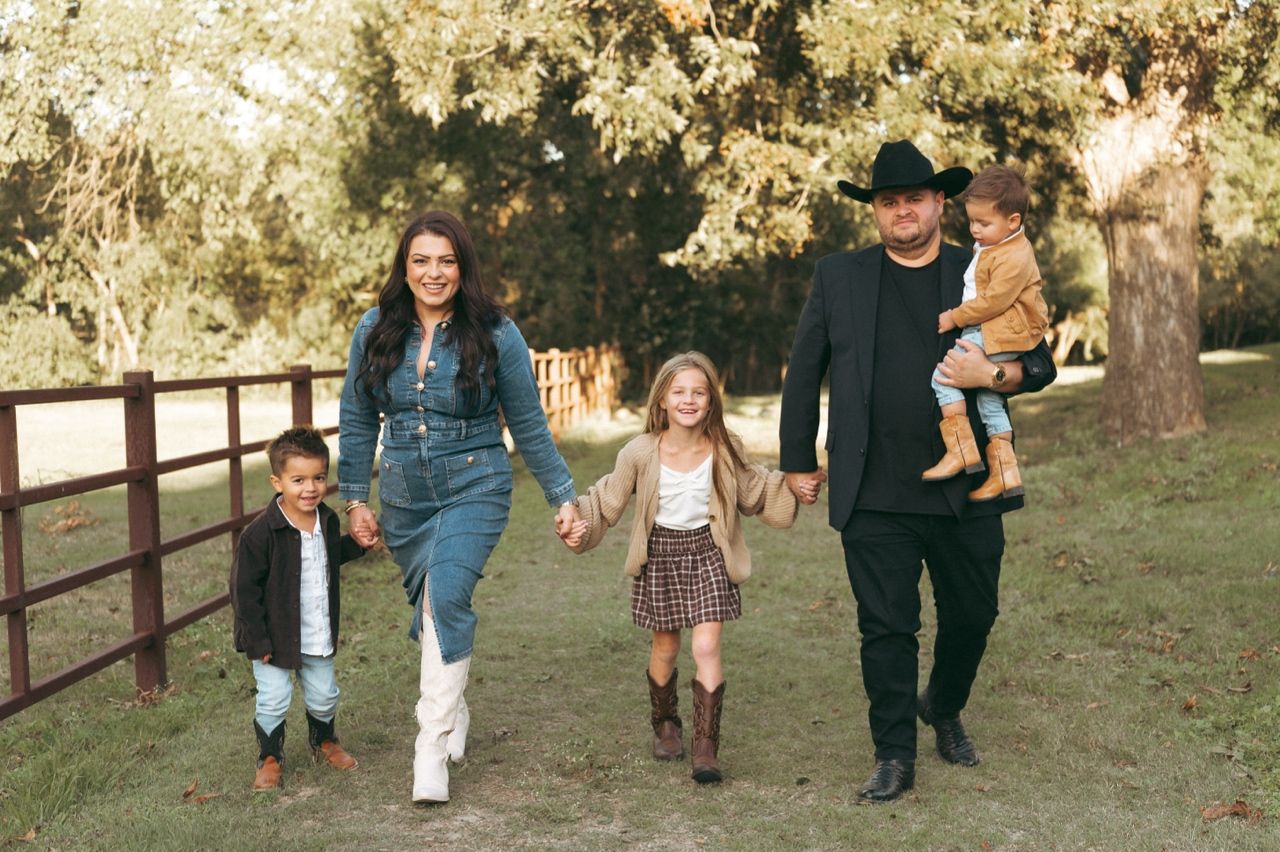 Smiling family of five in western outfits walks hand in hand across a grassy field at Windmill Stables.
