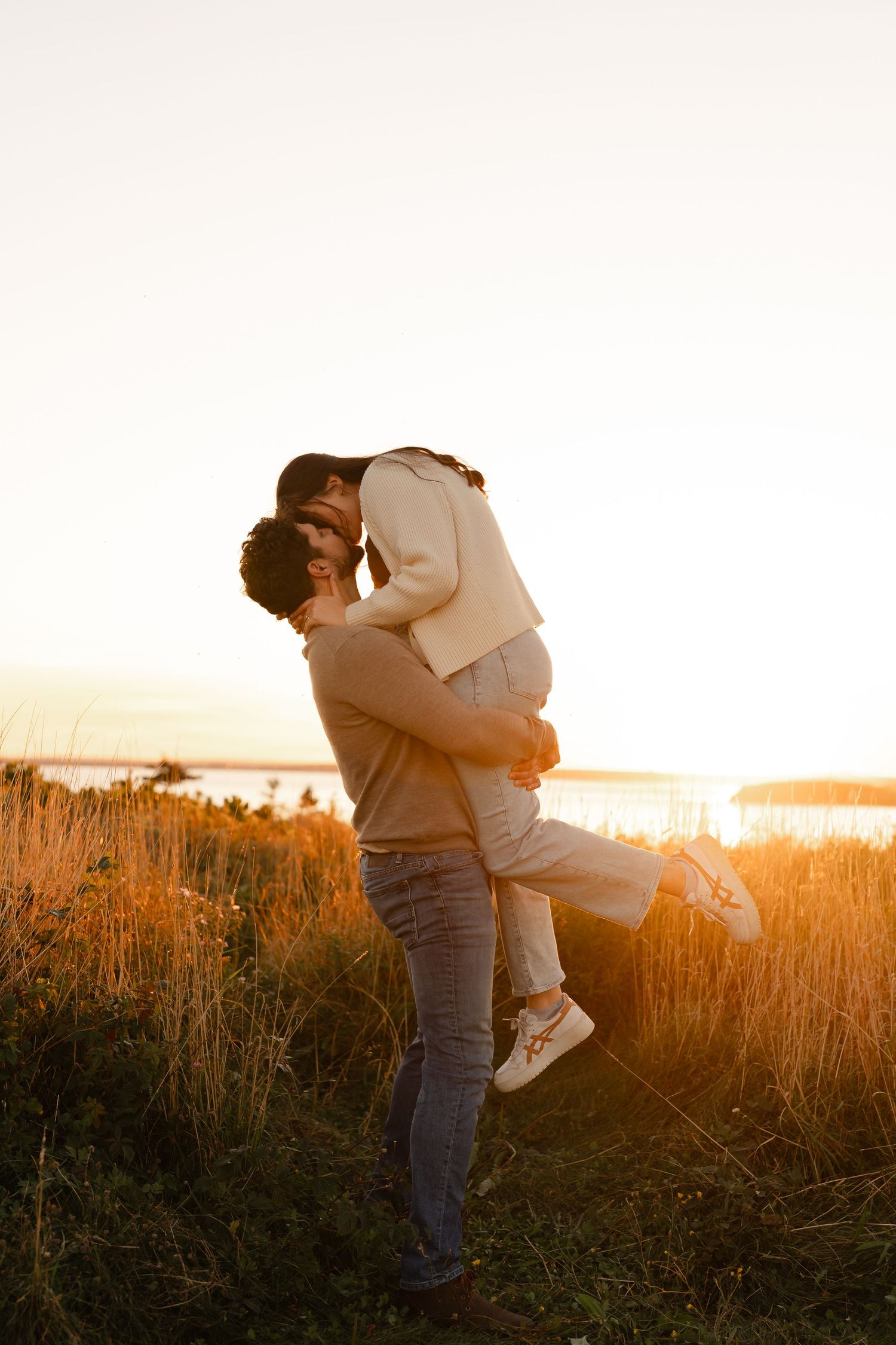 Couple sharing a romantic kiss at golden sunset, man lifting woman in a field near Laurencetown.