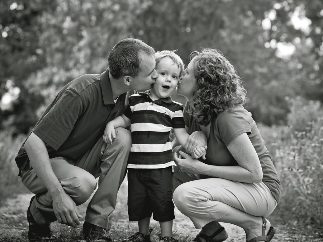 Black & white family portrait of parents kissing little boy during family photo session by Brighton, MI photographer